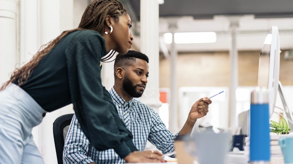 Focused black business woman working in the office with her colleague and using laptop.